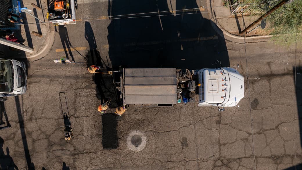 Vista aérea de trabajadores realizando labores de bacheo en una vialidad con apoyo de un camión de obra