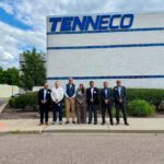 Grupo de siete personas frente a la fachada de una planta de Tenneco con el logotipo de la empresa visible en la parte superior del edificio.