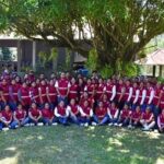 Grupo de personas con chalecos guinda reunidas al aire libre bajo un árbol