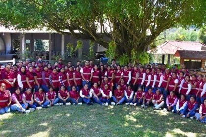 Grupo de personas con chalecos guinda reunidas al aire libre bajo un árbol