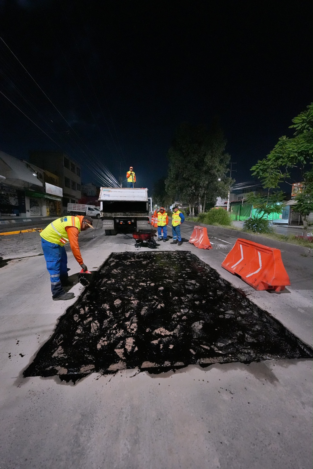 Trabajadores realizan labores nocturnas de mantenimiento vial y bacheo en una avenida del municipio de Querétaro.