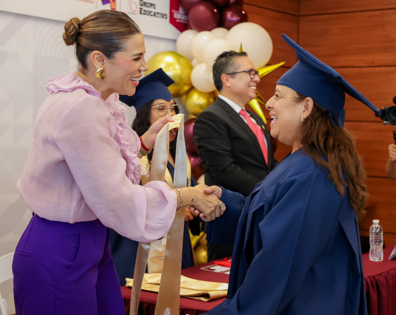 Marina del Pilar Avila Olmeda saluda a una mujer graduada durante un acto de certificación educativa en Baja California