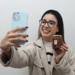 Joven emprendedora muestra un producto mientras toma una fotografía con su teléfono en Aguascalientes.