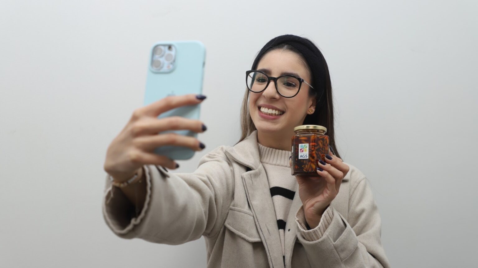 Joven emprendedora muestra un producto mientras toma una fotografía con su teléfono en Aguascalientes.
