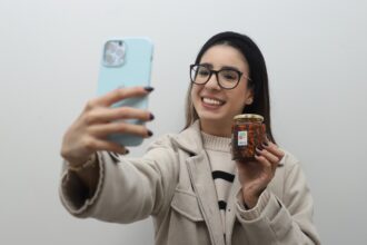 Joven emprendedora muestra un producto mientras toma una fotografía con su teléfono en Aguascalientes.