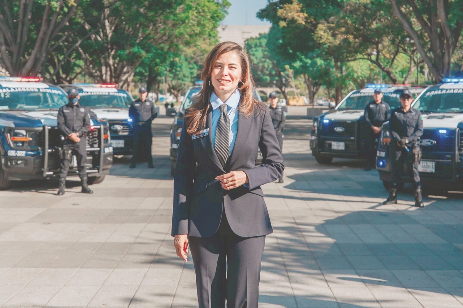 Presidenta municipal de Guadalajara durante una presentación sobre seguridad, con unidades y elementos policiales al fondo.