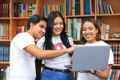 Tres jóvenes consultan una computadora portátil en una biblioteca.
