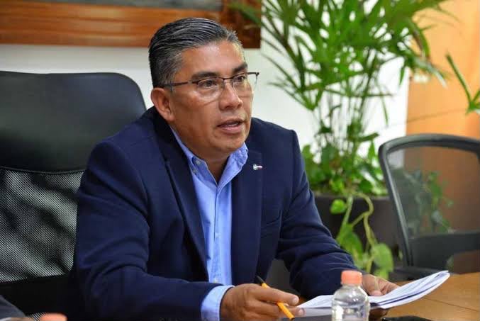 Hombre con traje oscuro y camisa azul durante una reunión de trabajo.
