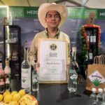 Representante de una marca de mezcal muestra un reconocimiento en el festival Mundo Mezcal 2026, junto a botellas de mezcal artesanal.