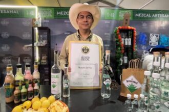 Representante de una marca de mezcal muestra un reconocimiento en el festival Mundo Mezcal 2026, junto a botellas de mezcal artesanal.