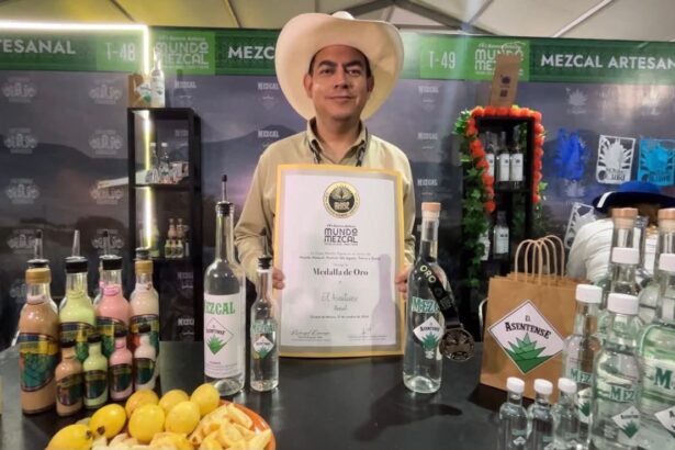 Representante de una marca de mezcal muestra un reconocimiento en el festival Mundo Mezcal 2026, junto a botellas de mezcal artesanal.
