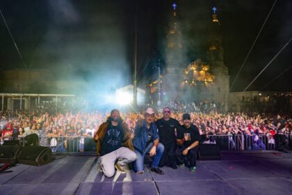 Integrantes de Plastilina Mosh y acompañantes posan sobre el escenario frente al público reunido en la Exedra de Aguascalientes durante el festival de aniversario.