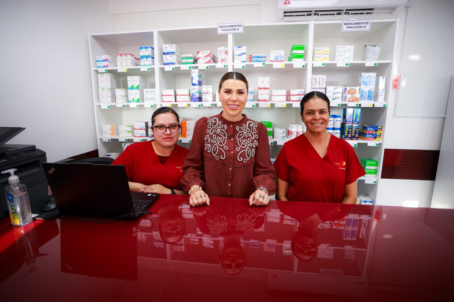 Tres mujeres posan en el mostrador de una Clínica del Bienestar, frente a estantes con medicamentos.