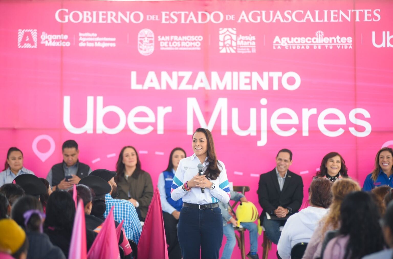 Una mujer habla ante el público durante el lanzamiento de Uber Mujeres en Aguascalientes, frente a un fondo rosa del evento.