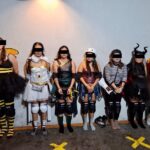Siete personas con disfraces y patines aparecen de pie ante una pared; sus ojos están cubiertos por franjas negras.