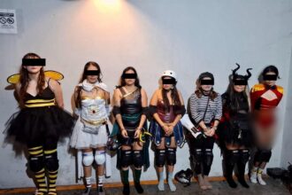 Siete personas con disfraces y patines aparecen de pie ante una pared; sus ojos están cubiertos por franjas negras.