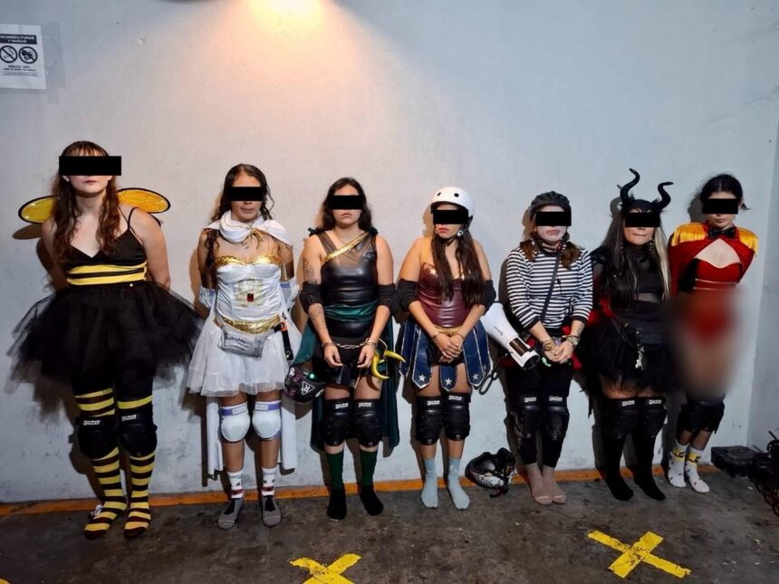 Siete personas con disfraces y patines aparecen de pie ante una pared; sus ojos están cubiertos por franjas negras.