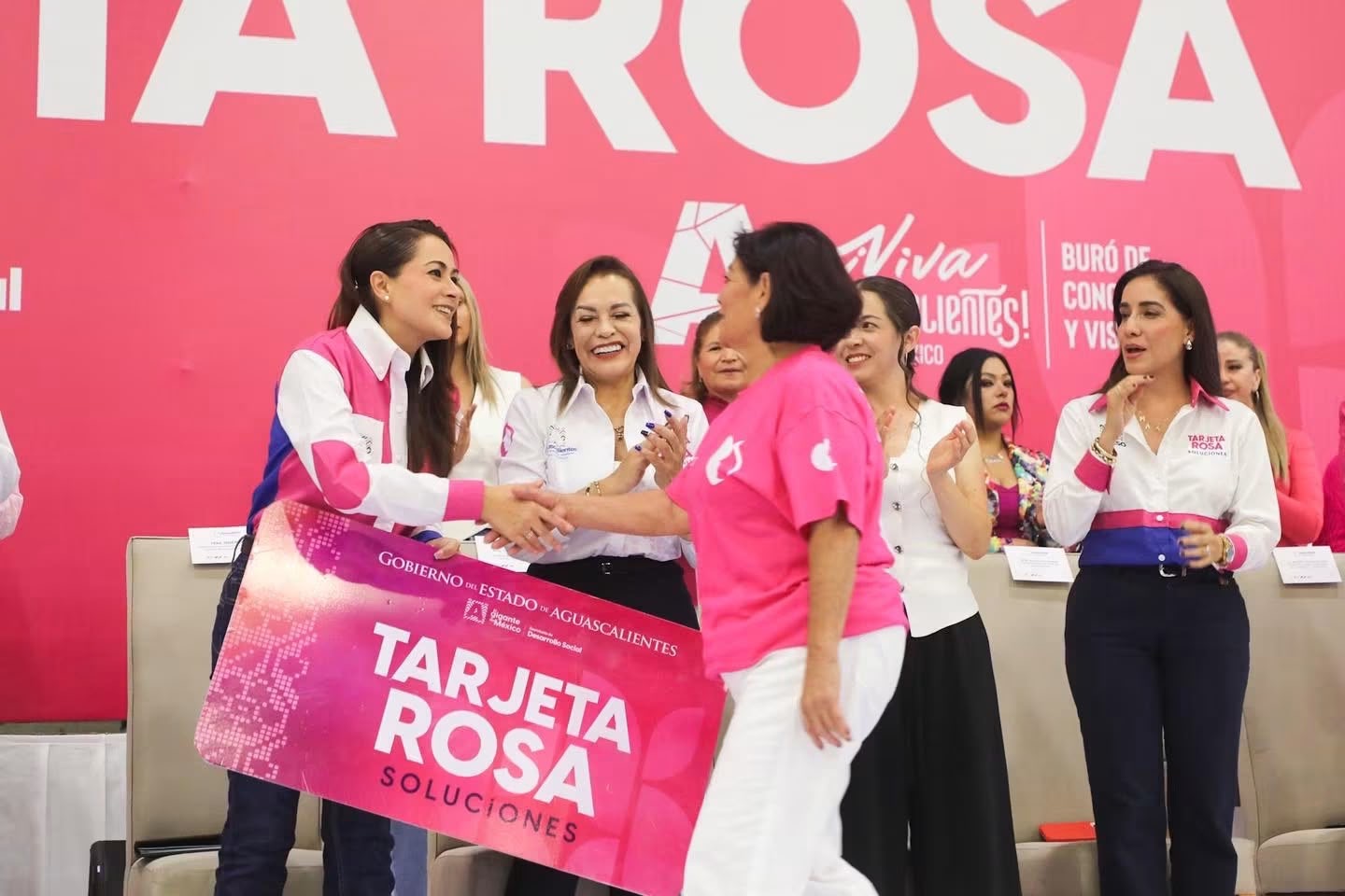 Durante un evento de Tarjeta Rosa en Aguascalientes, una funcionaria saluda a una beneficiaria frente a otras asistentes.