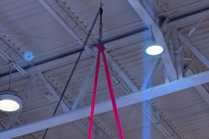 Atleta realiza una figura acrobática suspendida en telas aéreas rosas durante una competencia en un recinto deportivo.