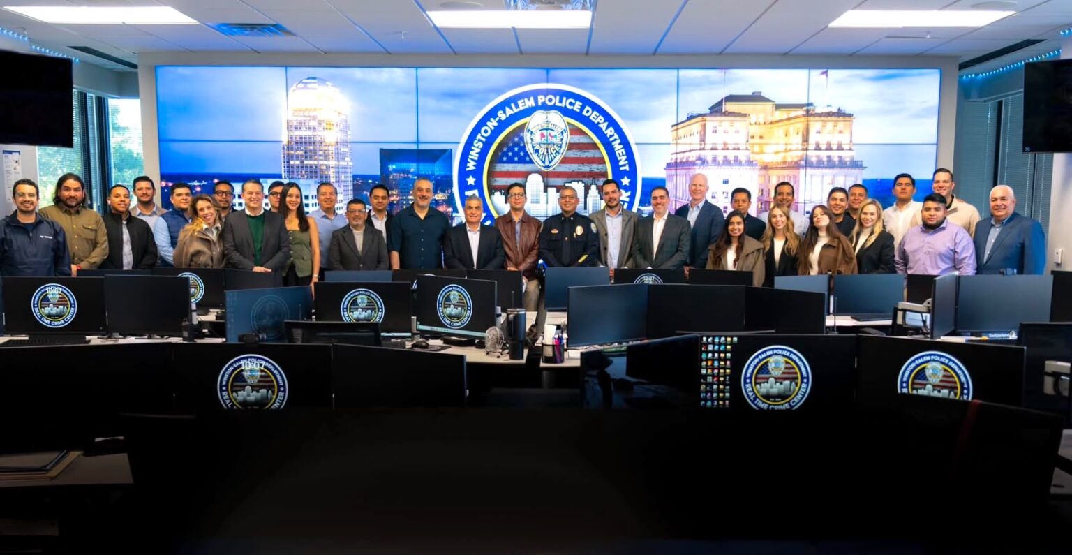 Delegación de visitantes y personal policial posan en el centro de monitoreo del Departamento de Policía de Winston-Salem, frente a pantallas y estaciones de trabajo