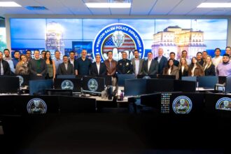 Delegación de visitantes y personal policial posan en el centro de monitoreo del Departamento de Policía de Winston-Salem, frente a pantallas y estaciones de trabajo