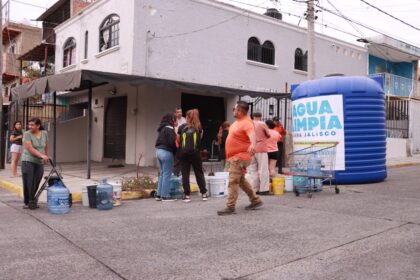 Habitantes se reúnen con recipientes para recibir agua junto a una cisterna azul con el letrero Agua Limpia para Jalisco en una calle de Guadalajara