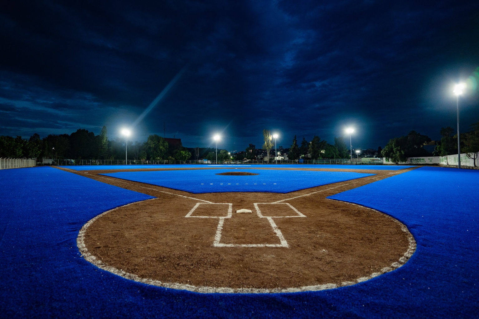 Campo de béisbol de la Unidad Deportiva Josefa Ortiz de Domínguez en Querétaro, con superficie azul e iluminación nocturna